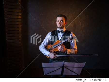 Violinist standing with instrument and bow behind music stand Violinist standing with instrument and bow behind music stand 141078365