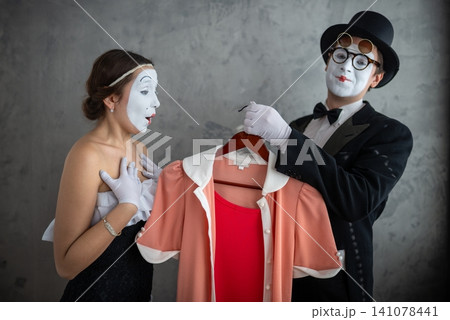Mime couple looking at a peach colored dress on a hanger Mime couple looking at a peach colored dress on a hanger 141078441
