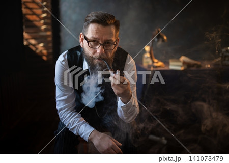 Elegant gentleman smoking a traditional pipe at his desk Elegant gentleman smoking a traditional pipe at his desk 141078479