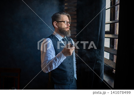 Intellectual man smoking a classic pipe by the window Intellectual man smoking a classic pipe by the window 141078499