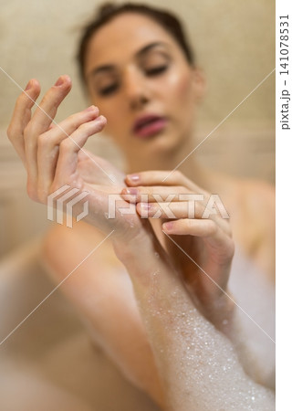 Woman examining soap foam on her hands in a tub 141078531