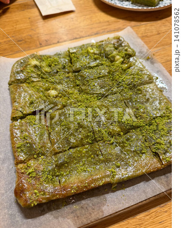 Traditional Turkish pistachio katmer dessert served on wooden table with generous pistachio topping. Turkish cuisine, gastronomy, food culture, dessert, hospitality, culinary tourism, authentic pastry Traditional Turkish pistachio katmer dessert served on wooden table with generous pistachio topping. Turkish cuisine, gastronomy, food culture, dessert, hospitality, culinary tourism, authentic pastry 141078562