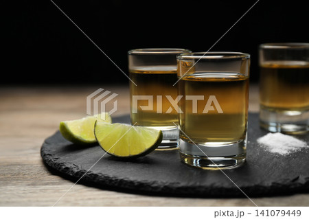 Mexican Tequila shots, lime slices and salt on wooden table 141079449