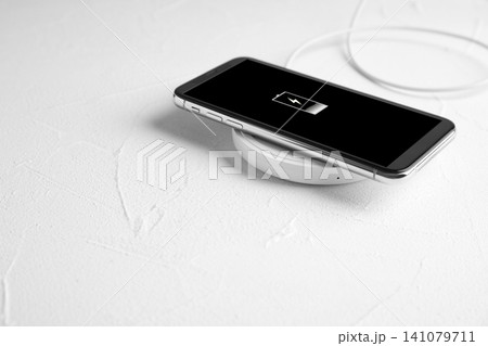 Mobile phone charging with wireless pad on white stone table. Space for text Mobile phone charging with wireless pad on white stone table. Space for text 141079711