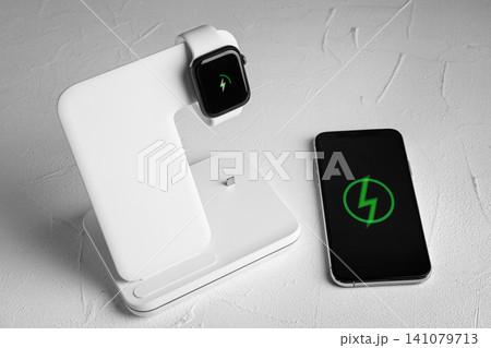 Smartwatch charging with wireless pad and mobile phone on white stone table Smartwatch charging with wireless pad and mobile phone on white stone table 141079713