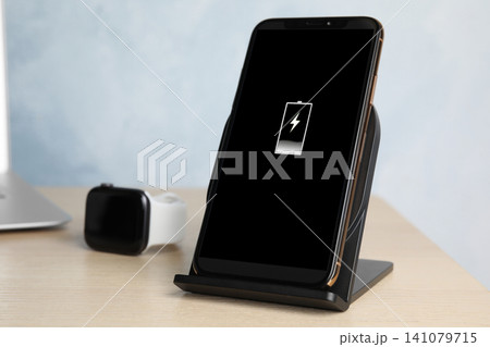 Mobile phone charging with wireless pad on wooden table, closeup 141079715
