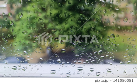 Raindrops on window glass with blurred green foliage background Raindrops on window glass with blurred green foliage background 141080081