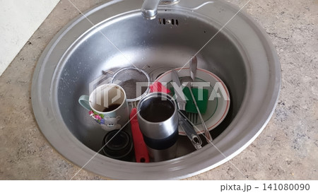 Dirty dishes piled in stainless steel kitchen sink with coffee cups and utensils Dirty dishes piled in stainless steel kitchen sink with coffee cups and utensils 141080090