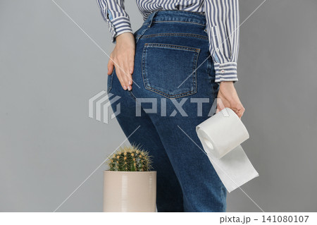 Woman with toilet paper sitting down on cactus against light grey background, closeup. Hemorrhoid concept Woman with toilet paper sitting down on cactus against light grey background, closeup. Hemorrhoid concept 141080107