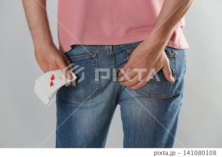 Man holding toilet paper with blood stain on light grey background, closeup. Hemorrhoid concept Man holding toilet paper with blood stain on light grey background, closeup. Hemorrhoid concept 141080108