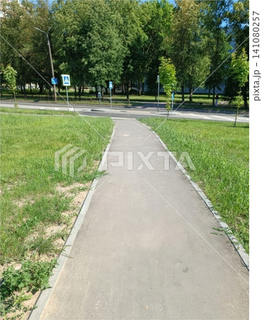 Paved pathway through green park with trees and road signs under sunny sky 141080257