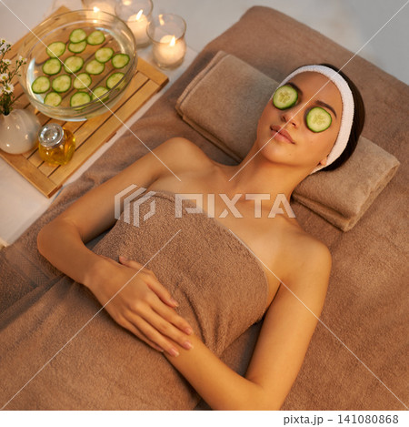 Top view, skincare and woman with cucumber on face at massage table in spa for peace, relax or wellness. Facial, above or person with vegetable on eyes for natural beauty or healthy organic treatment Top view, skincare and woman with cucumber on face at massage table in spa for peace, relax or wellness. Facial, above or person with vegetable on eyes for natural beauty or healthy organic treatment 141080868