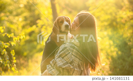 Smiling Woman Holding Beagle During Golden Hour Walk Smiling Woman Holding Beagle During Golden Hour Walk 141081131