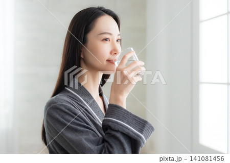 窓辺で水を飲む若い女性　  141081456