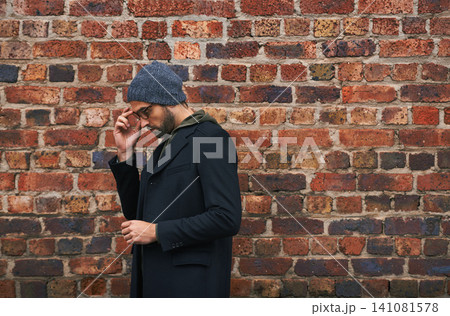 Fashion, man and thinking on brick wall with glasses for trendy, cool and style for urban with idea. Male person, outdoor and planning for weekend or holiday with winter outfit and stylish in Germany 141081578