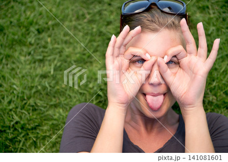 Portrait, hand glasses and woman with tongue out for funny face, goofy or silly in outdoor garden. Top view, comic and female person joking for humor, finger shape gesture and playful mood in park Portrait, hand glasses and woman with tongue out for funny face, goofy or silly in outdoor garden. Top view, comic and female person joking for humor, finger shape gesture and playful mood in park 141081601
