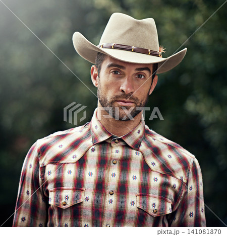 Man, portrait and outdoor cowboy outfit, western culture and countryside ranch in Texas. Male person, hat and flannel trend for farmer aesthetic, nature and plaid style by trees or outside bush 141081870