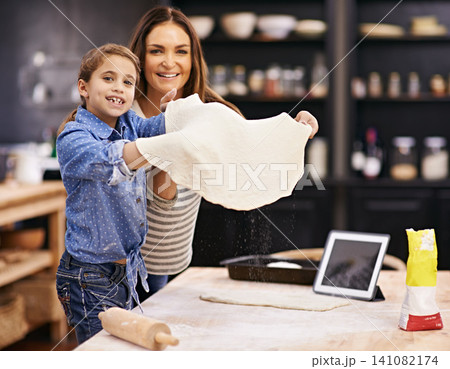 Portrait, mother or child baking pizza in a kitchen teaching recipe for help, support or learning in home. Kid, tablet or girl cooking with parent, family and mom for dinner, supper or lunch together 141082174