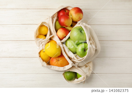 Cotton eco bags with fruits on white wooden background, flat lay Cotton eco bags with fruits on white wooden background, flat lay 141082375