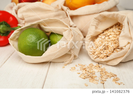 Cotton eco bags with fruits and oat flakes on white wooden table, closeup 141082376