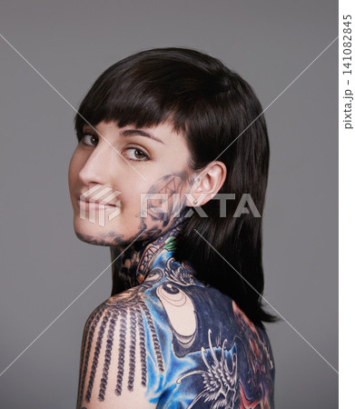 Happy woman, portrait and beauty with back tattoo for haircare, style or facial treatment on a gray studio background. Face of female person, young model or smile for body art, design or creativity Happy woman, portrait and beauty with back tattoo for haircare, style or facial treatment on a gray studio background. Face of female person, young model or smile for body art, design or creativity 141082845