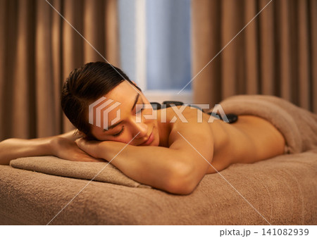 Sleep, woman and massage with stone at spa for luxury self care, organic body health and wellness. Towel, table and female person with peace for hot rock therapy, stress relief and spiritual healing 141082939