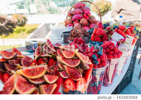 Fresh cut fruit served in clear plastic cups at an outdoor market stall. Seasonal summer produce offers healthy refreshments and ready to eat street food. Fresh cut fruit served in clear plastic cups at an outdoor market stall. Seasonal summer produce offers healthy refreshments and ready to eat street food. 141083088