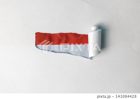 A creative studio shot featuring a clean white sheet of paper with a torn section in the middle, revealing a textured red and white fabric flag underneath. This visual metaphor represents discovering A creative studio shot featuring a clean white sheet of paper with a torn section in the middle, revealing a textured red and white fabric flag underneath. This visual metaphor represents discovering 141084428