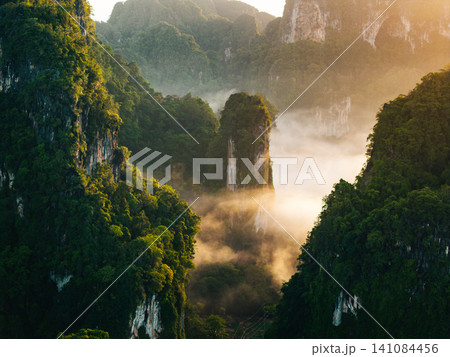 Golden morning sunlight illuminating misty limestone karst peaks in tropical rainforest, Krabi. 141084456