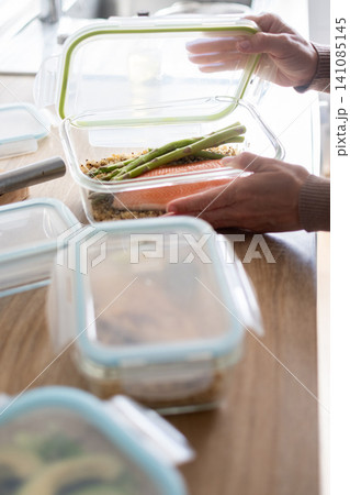 Woman opening a healthy salmon meal prep container in the kitchen 141085145