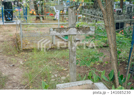 Wooden cross standing upright, in cemetery, with wooden cross, metal fence, flowers, trees, with wood, metal texture, from a ground-level perspective perspective. 141085230