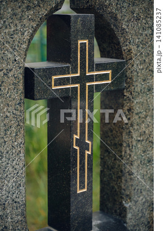 serene grave marker with cross in granite cemetery close-up with black and gold accents, solemn and peaceful setting for religious memorial use cases and editorial content. 141085237