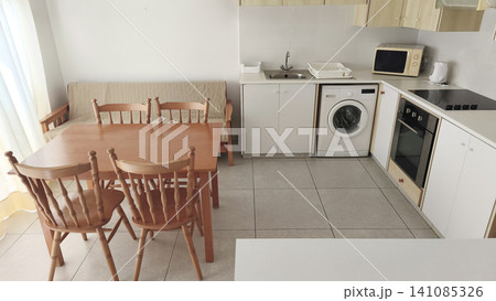 Bright modern apartment kitchen with dining area, wooden furniture and fully equipped appliances. Cozy holiday rental interior designed for comfortable everyday living. Bright modern apartment kitchen with dining area, wooden furniture and fully equipped appliances. Cozy holiday rental interior designed for comfortable everyday living. 141085326