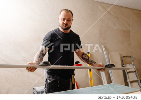 Construction worker using suction cups lifting drywall sheet during renovation works Construction worker using suction cups lifting drywall sheet during renovation works 141085438