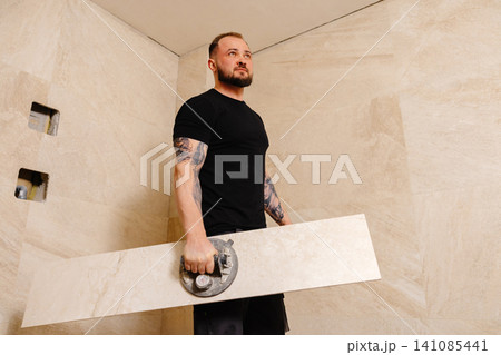 Tiler installing large format tile on bathroom wall using suction cup Tiler installing large format tile on bathroom wall using suction cup 141085441