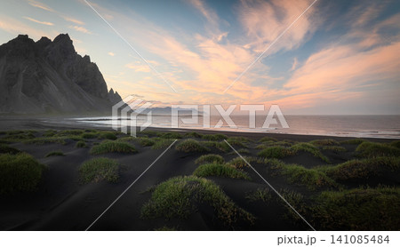 Colorful sunset over the iconic Vestrahorn mountain with black volcanic sand dunes and the Atlantic coastline. Peaceful Icelandic landscape with dramatic sky and untouched nature. Colorful sunset over the iconic Vestrahorn mountain with black volcanic sand dunes and the Atlantic coastline. Peaceful Icelandic landscape with dramatic sky and untouched nature. 141085484