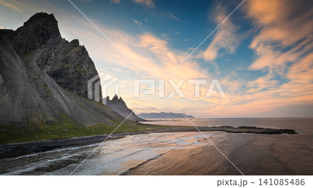 Aerial view of the dramatic Vestrahorn mountain rising above the black volcanic coastline during a colorful sunset. Rugged cliffs, Atlantic Ocean and untouched Icelandic wilderness. 141085486