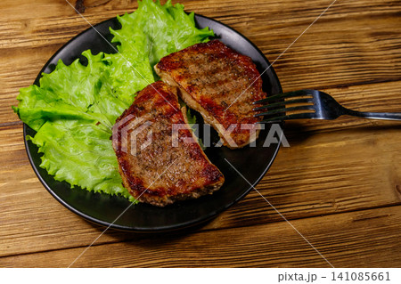Grilled pork steaks with lettuce leaves on wooden table Grilled pork steaks with lettuce leaves on wooden table 141085661