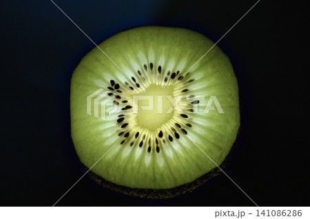 Backlit kiwi fruit slice glowing against a dark background. Backlit kiwi fruit slice glowing against a dark background. 141086286
