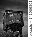 Black and white shot of an abandoned industrial headframe tower under dark sky. 141086301