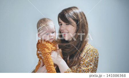 Loving mother tenderly embracing newborn daughter, sharing warm connection against soft blue backdrop 141086368