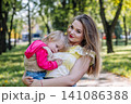Nurturing mother embracing tearful child, offering solace amid lush park landscape, sunlight warming tender moment 141086388