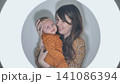 Loving mother tenderly embracing smiling infant, radiating maternal warmth inside soft luminous background 141086394