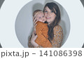Young mother holding her baby, posing joyfully for a photo shoot inside a ring light, capturing the warmth of their tender bond 141086398