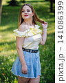 Fashionable young woman wearing a light yellow blouse and a denim skirt, touching her hair in a park, enjoying a sunny summer day 141086399