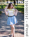 Youthful woman relaxing in urban park, sporting trendy denim skirt and breezy top, radiating summer confidence and casual chic style 141086401