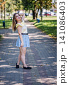 Stylish female confidently standing amid lush greenery, basking in warm sunlight during bright summer afternoon 141086403