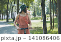 Young woman enjoying a sunny day riding an electric scooter in a green park, embracing sustainable transportation and outdoor leisure 141086406