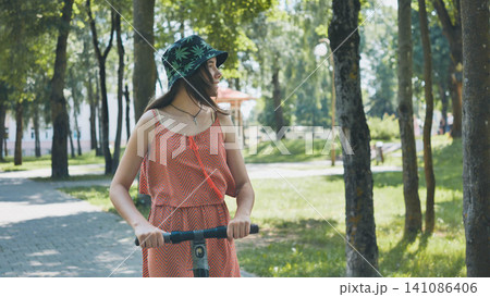 Young woman enjoying a sunny day riding an electric scooter in a green park, embracing sustainable transportation and outdoor leisure Young woman enjoying a sunny day riding an electric scooter in a green park, embracing sustainable transportation and outdoor leisure 141086406