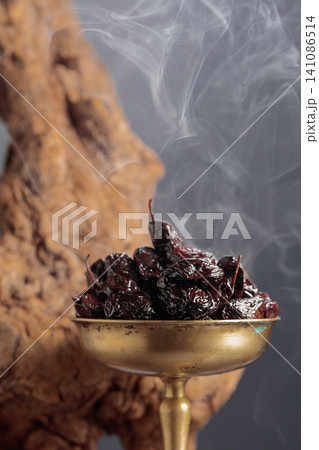 Dry cured black olives in a vintage brass bowl on a background of weathered olive tree snags. Dry cured black olives in a vintage brass bowl on a background of weathered olive tree snags. 141086514